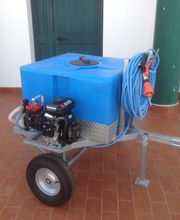 Carrello con serbatoio blu, motore e tubo arrotolato su pavimento in mattoni rossi.