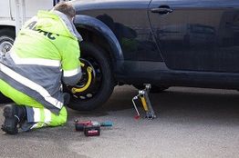 Mechanic in reflective gear changing a car tire on a roadside.