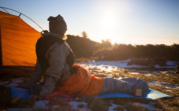 Frau liegt im Schnee während einem Sonnenuntergang