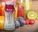 Bottle of Zurvita Zeal drink mix with fresh fruits and smoothies in the background.
