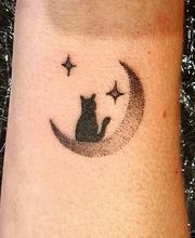 Tattoo van een kat op een halve maan met sterren eromheen op iemands arm.
