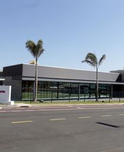 Centro tecnológico moderno com fachada de vidro, cercado por palmeiras à beira de uma estrada asfaltada.