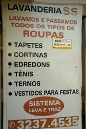 Placa de lavanderia oferecendo serviços para tapetes, cortinas, edredons, tênis, ternos e vestidos.