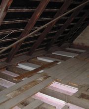 Dachboden mit Holzbalken und Isolierung; Dachfenster, lose Kabel sichtbar.