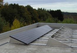 Solarmodul auf einem Flachdach, umgeben von Bäumen und bewölktem Himmel im Hintergrund.