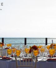 Bodas al aire libre con vista al mar, mesas elegantes y copas amarillas al atardecer.