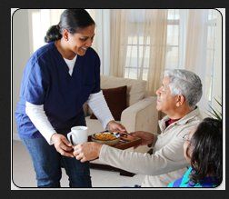 Caregiver serving food and drink to an elderly man seated with a child in a cozy living room.