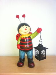 Marienkäfer-Figur mit Laterne auf Holzoberfläche, lächelt freundlich.