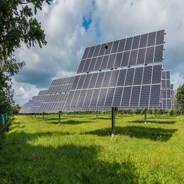 Rows of solar panels in a grassy field under a cloudy sky.