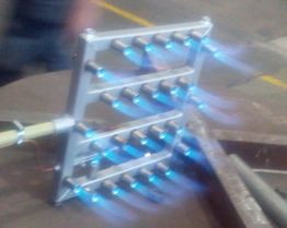 Bruciatore a gas multiplo acceso con fiamme blu in un ambiente industriale.