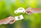 Hands exchanging a paper car and money symbol on a green background.