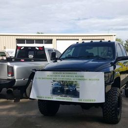 Two pickup trucks parked, one with a Sumner Automotive service banner on the front.