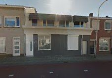 Rij van huizen met etalageramen en gesloten luiken onder blauwe lucht.