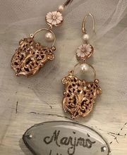 Goldene Ohrringe mit Perlen und Blumenmotiv, auf Holzplatte mit Schriftzug "Marino Lugano".