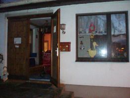 Geöffnetes Holztor eines Hauses, Kinderwagen drinnen, Fenster mit Enten-Deko und Gardinen.