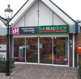 Winkelpand met de borden: Drogerij & Parfumerie en The Read Shop Express, op een bestraat terrein.