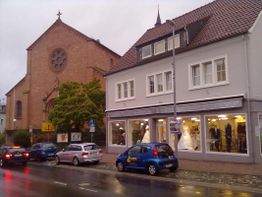 Straßenansicht mit Kirche, Geschäft und Autos bei regnerischem Wetter, Schaufenster mit Brautkleid.