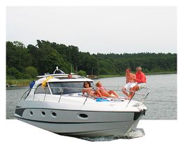 Menschen entspannen auf einem Boot auf einem ruhigen See mit bewaldetem Ufer im Hintergrund.
