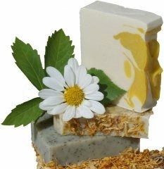 Drei Seifenstücke mit Kamillenblume und Blättern verziert, auf Heu liegend.