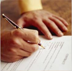 Eine Hand unterschreibt ein Dokument mit einem Stift, die andere Hand liegt auf dem Tisch.