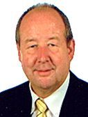 Ein lächelnder Mann in Anzug und Krawatte vor weißem Hintergrund.