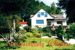 Ferienwohnung mit Garten, umgeben von Bäumen. Text: "Ferienwohnung Stefan" in roter Schrift.
