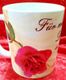 Weiße Tasse mit roter Rose und dem Schriftzug "Für meine Darling" auf rotem Stoffhintergrund.