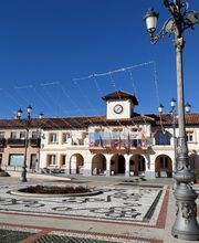 Plaza con farolas, edificio con reloj y cielo azul.