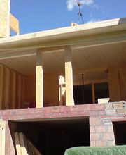 Teilweise gebautes Haus mit Holzwänden und offenem Dach unter blauem Himmel.