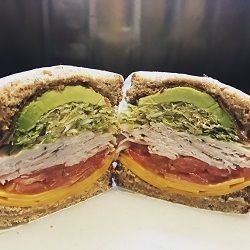 A sliced sandwich with turkey, cheese, tomato, lettuce, and avocado on whole-grain bread.