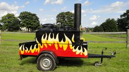 Anhänger mit aufgemalter Flamme, Auspuff und grüne Wiese im Hintergrund.