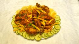 Gegrilltes Hähnchen mit Pommes, dekoriert mit Zitronenscheiben und Gurken auf weißem Teller.