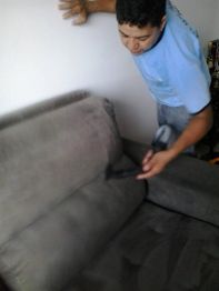 Homem aspirando sofá cinza com aspirador de pó.