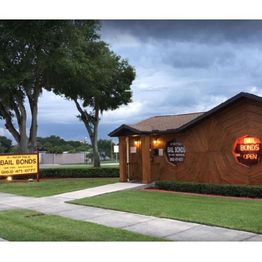 Bail bonds office with neon sign, surrounded by green lawn and trees against a cloudy sky.