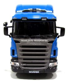 Caminhão azul visto de frente com logotipo "Transleste Transportes" e marca "Scania" visíveis.