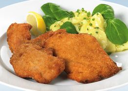Paniertes Schnitzel mit Kartoffelpüree und Spinatblättern auf einem weißen Teller.