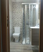 Baño moderno con ducha de vidrio, inodoro, lavabo y pared de azulejos grises y blancos.