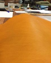 Mesa de trabajo con telas, piel naranja extendida y objetos variados en el fondo.