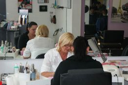 Zwei Frauen in einem Friseursalon, eine sitzt am Tisch, Spiegelbild im Hintergrund.
