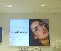 Poster aan de muur van een opticien met merklogo en een vrouw die een bril draagt.