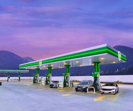 Estación de servicio bajo un cielo rosado, con coches en las bombas de gasolina.
