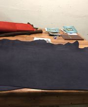 Mesa de trabajo con cuero azul extendido, papeles, y herramientas al fondo.