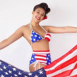 Person in a stars and stripes swimsuit holding a matching flag, smiling.