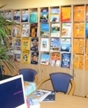 Reisebüro mit Broschürenwand, Computer und Pflanze auf einem Tisch.