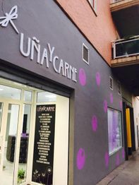 Fachada de tienda "Uña y Carne" con decoración de lunares morados en una calle estrecha.