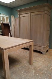 Houten tafel en kast in een kamer met groene muren. Er staan planken tegen de muur.