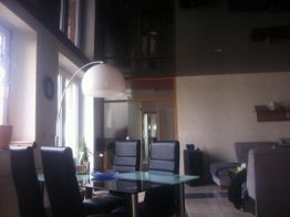 Wohnzimmer mit Glas-Esstisch, schwarzen Stühlen und Stehlampe, daneben großes Fenster.