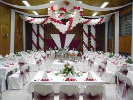 Festlich dekorierter Saal mit weißen und roten Ballons, gedeckte Tische und Hochzeitsstühlen.