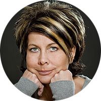Frau mit kurzem Haar und Strähnen, stützt das Kinn auf die Hände, ernst guckend.