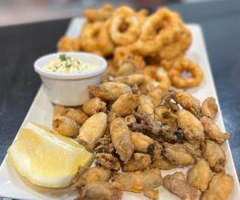 Plato de calamares y pescaditos fritos con mayonesa y limón en un plato blanco.